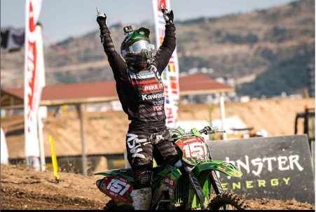 Courtney Duncan celebrates a win with two hands in the air as she sits astride her muddy motocross bike