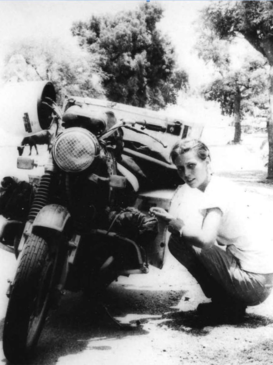 Elspeth Beard, first British woman to ride around the world, kneeling next to her motorbike